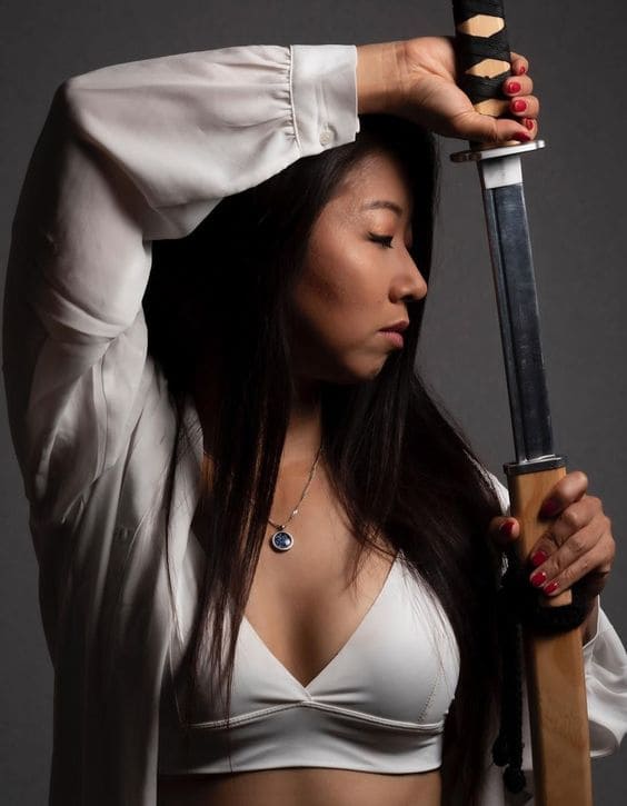girl unsheathing katana overhead pose with eyes closed while looking to the left